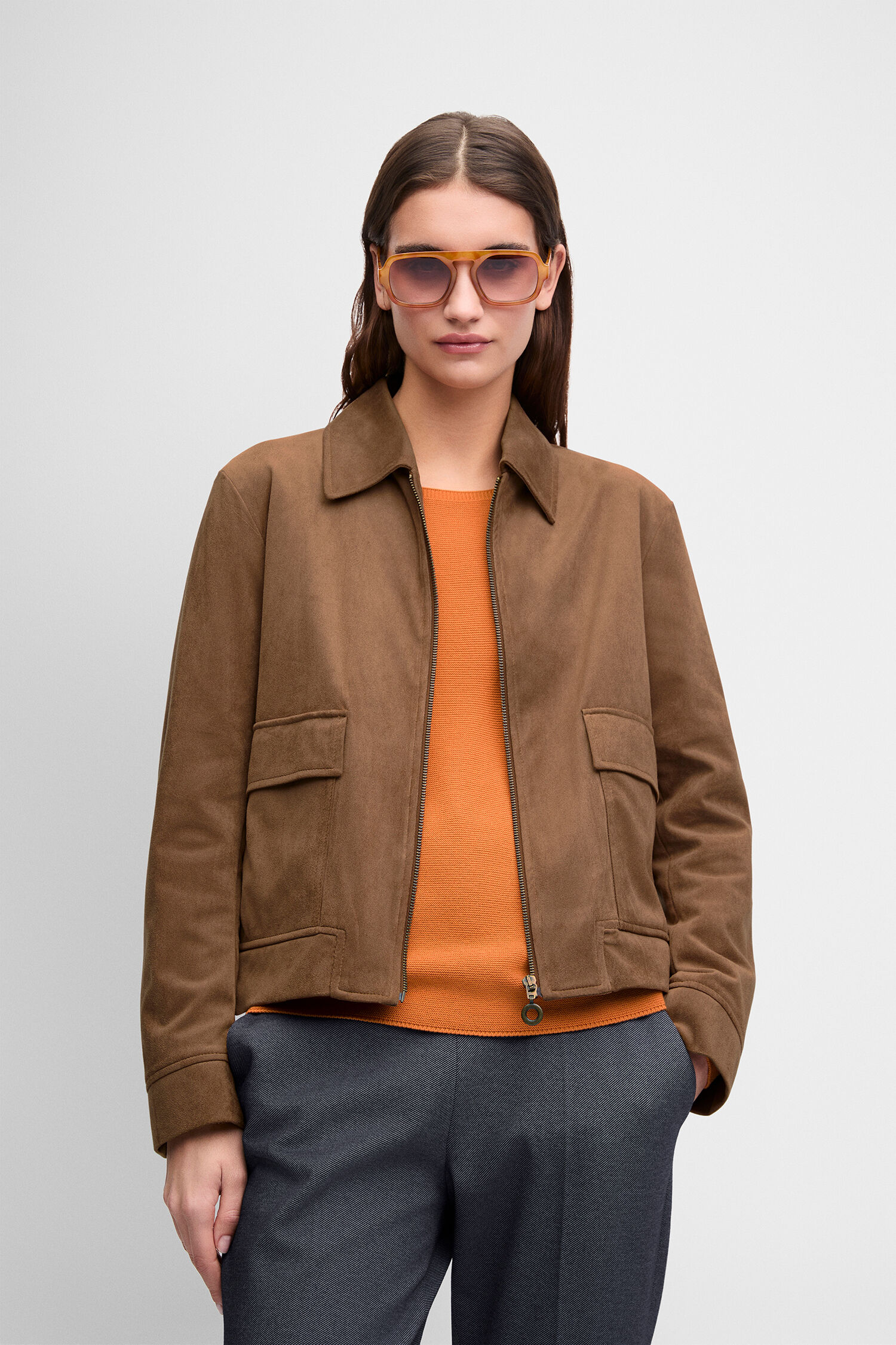 braune Wildlederjacke, orangefarbene Pullover, dunkle Hose, Stiefeletten, Sonnenbrille